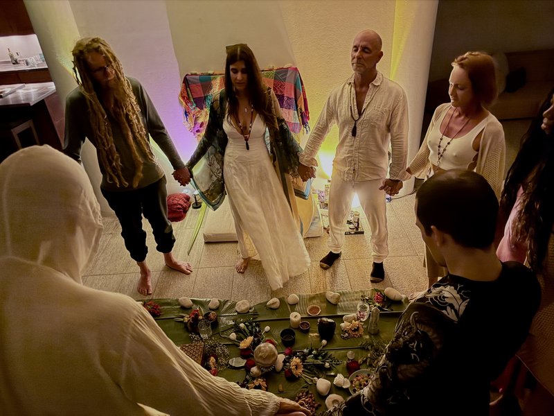 Night ceremony at Casa Cielo: participants standing in a circle holding hands around a banana-leaf altar with candles and stones